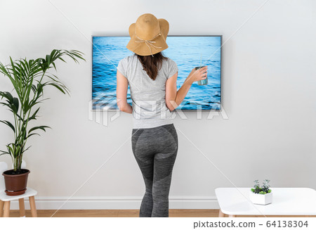 Woman at home pretending to be on the beach. TV screen. 2020 summer quarantine travel. Stay home Woman at home pretending to be on the beach. TV screen. 2020 summer quarantine travel. Stay home 64138304