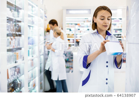 Attentive female pharmacist reading the composition of the drug. 64138907