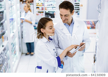 Two pharmacists checking the availability of medicines in a pharmacy. 64138909