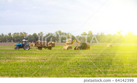 Tractor loading hay bales on truck agricultural works 64142399