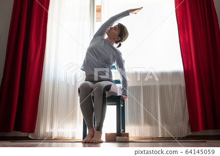 Young cheerful woman practicing yoga, sitting on chair doing side bend exercise Young cheerful woman practicing yoga, sitting on chair doing side bend exercise 64145059