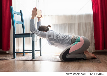 Woman stretching and opening shoulders using chair at the living room. Woman stretching and opening shoulders using chair at the living room. 64145062