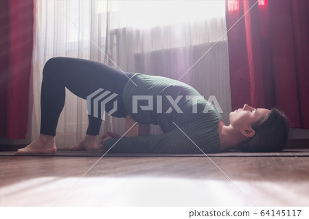 Caucasian young woman doing yoga exercise ardha chakrasana 64145117