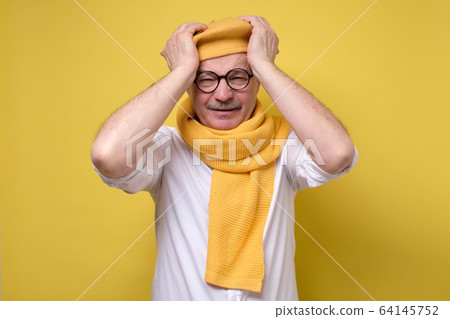 senior man in funny beret and scarf having headache 64145752