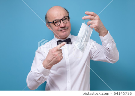 Young caucasian man with mustache pointing on a medical mask. Young caucasian man with mustache pointing on a medical mask. 64145756