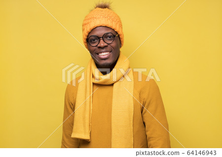 Young african man in yellow sweater hat and scarf smiling looking at camera Young african man in yellow sweater hat and scarf smiling looking at camera 64146943