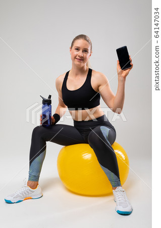 slim fit blonde girl in a fitness uniform is engaged in fitness on a gray background slim fit blonde girl in a fitness uniform is engaged in fitness on a gray background 64147034