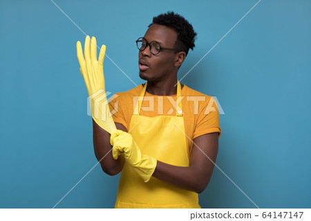 Young african american man cleaning using gloves standing on yellow wall 64147147
