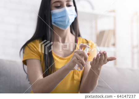 Coronavirus prevention. Young girl in medical mask applying sanitizer on her hands at home 64147237