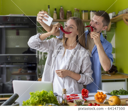 Happy young couple fooling in the kitchen with chili pepper Happy young couple fooling in the kitchen with chili pepper 64147300
