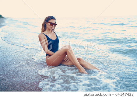 portrait of beautiful sexy caucasian sunbathed woman in leopard print sunglasses with long hair in swimsuit lying on summer beach 64147422