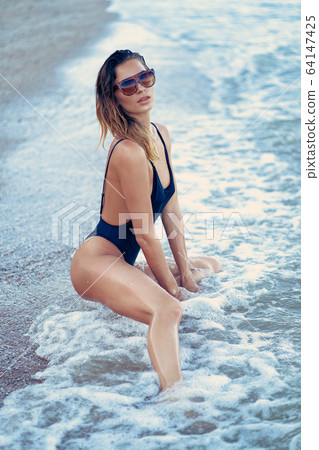 portrait of beautiful sexy caucasian sunbathed woman in leopard print sunglasses with long hair in swimsuit lying on summer beach 64147425