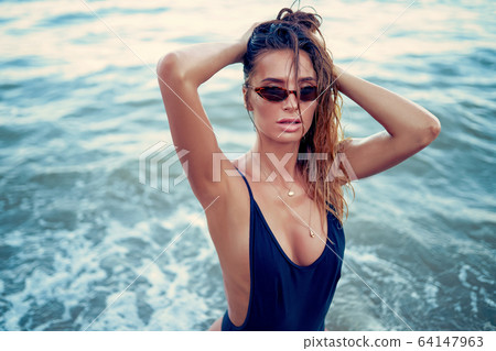 portrait of beautiful sexy caucasian sunbathed woman in leopard print sunglasses with long hair in swimsuit lying on summer beach 64147963
