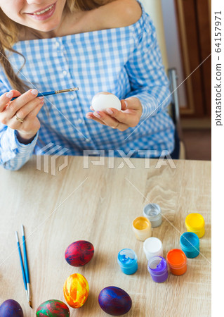 Holidays, handmade and creation concept - Happy young woman draws on Easter egg, close-up. 64157971