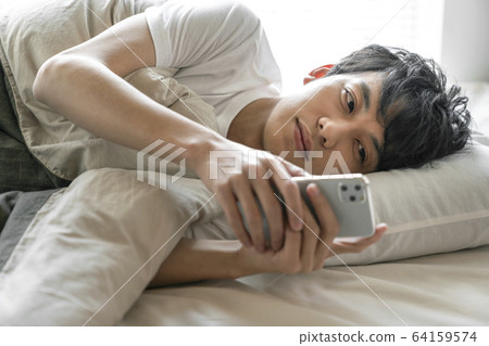 Young man looking at smartphone while sleeping 64159574