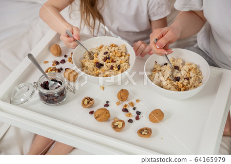 Happy mom and daughter have healthy breakfast on bed in a light bedroom on a sunny morning. Oatmeal Happy mom and daughter have healthy breakfast on bed in a light bedroom on a sunny morning. Oatmeal 64165979