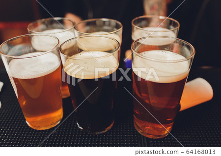 Friends cheering with beer glasses sitting around cafe bar table - Group of multiracial people toasting and clinking drinks at each others health inside pub - Vintage nostalgic old times filter look. 64168013