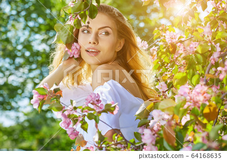 Beautiful young woman walking near the blossoming Beautiful young woman walking near the blossoming 64168635