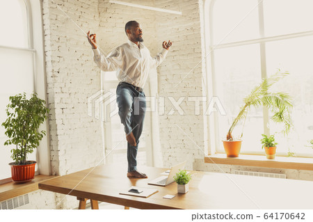 Young african-american man doing yoga at home while being quarantine and freelance working 64170642