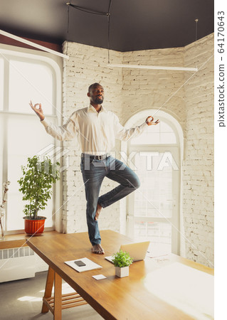 Young african-american man doing yoga at home while being quarantine and freelance working Young african-american man doing yoga at home while being quarantine and freelance working 64170643