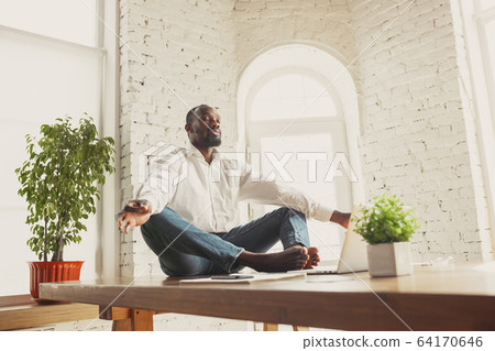 Young african-american man doing yoga at home while being quarantine and freelance working 64170646
