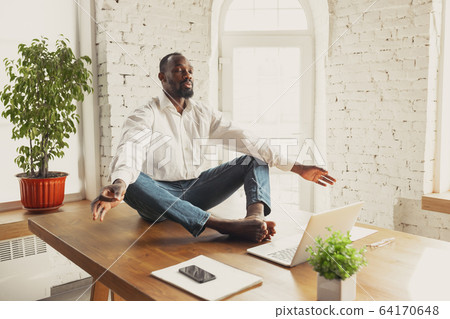 Young african-american man doing yoga at home while being quarantine and freelance working Young african-american man doing yoga at home while being quarantine and freelance working 64170648