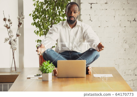 Young african-american man doing yoga at home while being quarantine and freelance working 64170773