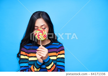 Young woman hides her face behind colorful lollipop isolated on blue background 64171336