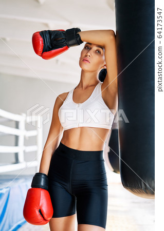 Sporty tiired woman wearing boxing gloves posing in gym Sporty tiired woman wearing boxing gloves posing in gym 64173547