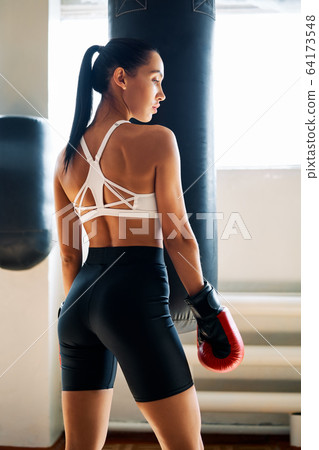 Back view of sporty young woman in boxing gloves posing in gym Back view of sporty young woman in boxing gloves posing in gym 64173548