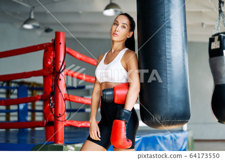 Sporty young woman wearing boxing gloves posing in gym Sporty young woman wearing boxing gloves posing in gym 64173550