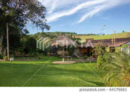 An yard of a small farm. It has a barbecue area with clay tiles, a thatched roof and a large grass field An yard of a small farm. It has a barbecue area with clay tiles, a thatched roof and a large grass field 64176661