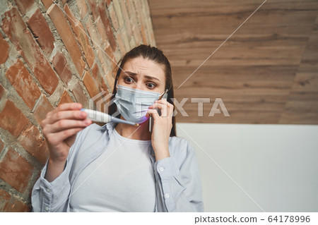 Scared young Caucasian female holding a thermometer 64178996