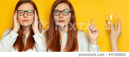 Stress, headache concept. Young woman worker in glasses touches her head. The girl raised her finger up, female hand holds a glass of water on a yellow background Stress, headache concept. Young woman worker in glasses touches her head. The girl raised her finger up, female hand holds a glass of water on a yellow background 64180682