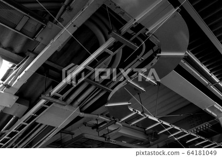 Monochrome photo of power distribution and plumbing equipment installed on the ceiling of an industrial facility with a complex structure Monochrome photo of power distribution and plumbing equipment installed on the ceiling of an industrial facility with a complex structure 64181049