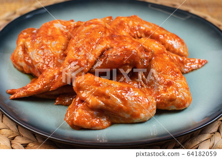 Marinated chicken wings on a blue dark plate,Chicken wings are raw in the marinade. 64182059