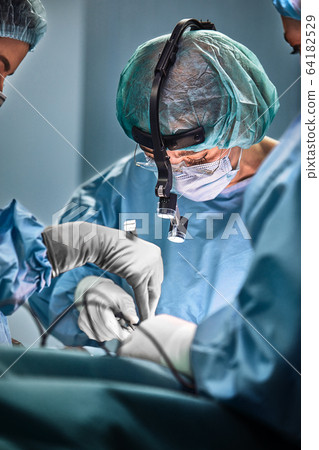 In the hospital operating room. An international team of professional surgeons and assistants works in a modern operating room. Professional doctors celebrate successfully saved lives. 64182529