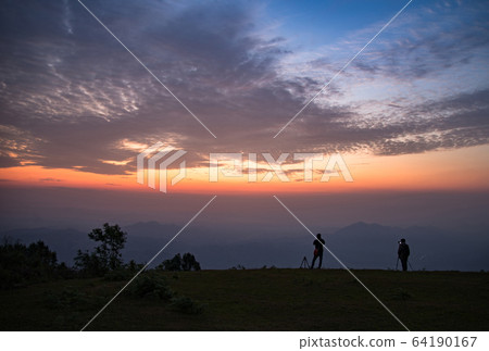 Photographer man standing on hill with sunrise landscape mountain fog mist colorful sky beautiful clouds in the morning silhouettes 64190167