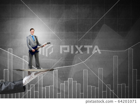 Businessman on metal tray playing electric guitar against graphs background Businessman on metal tray playing electric guitar against graphs background 64201071