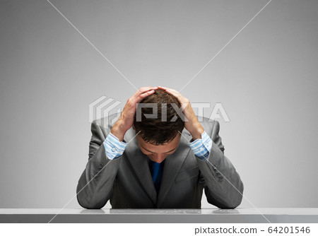 Frustrated man sitting at desk with hands on head 64201546