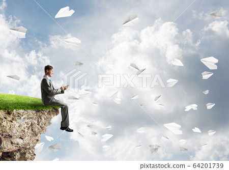 Elegant businessman on rock edge making calls and paper planes flying around Elegant businessman on rock edge making calls and paper planes flying around 64201739