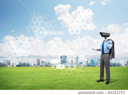 Camera headed man standing on green grass against modern cityscape 64201755