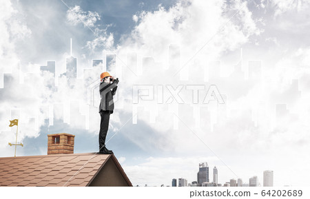 Engineer man standing on roof and looking in binoculars. Mixed m 64202689