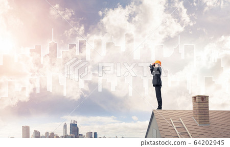 Engineer man standing on roof and looking in binoculars. Mixed m 64202945