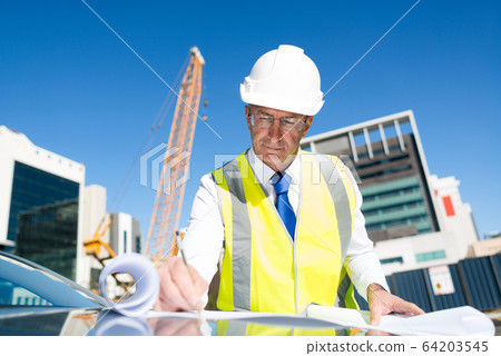 Senior foreman in glasses doing his job at building area on car hood Senior foreman in glasses doing his job at building area on car hood 64203545