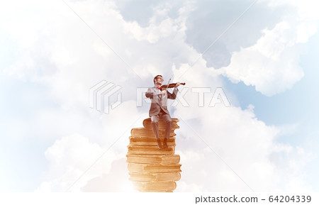 Handsome violinist in blue day sky on pile of books play his melody Handsome violinist in blue day sky on pile of books play his melody 64204339