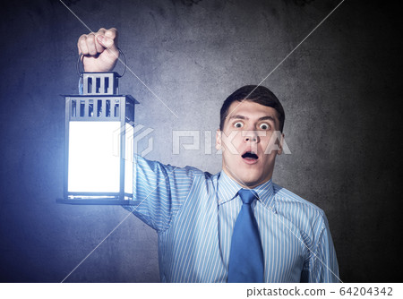 Horrified businessman holding glowing lantern Horrified businessman holding glowing lantern 64204342