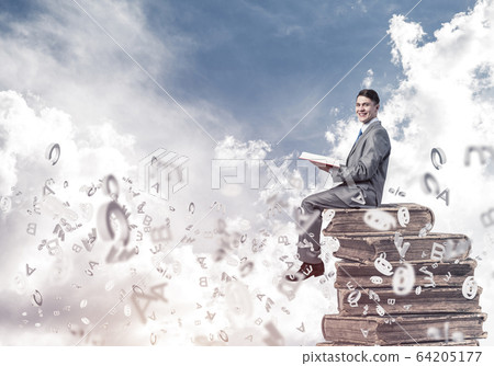 Man student on stack reading book and symbols flying around 64205177