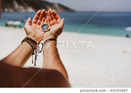 Man's hand holding compass. Beach and sea in background The concept of travel, summer vacation, holiday and journey Man's hand holding compass. Beach and sea in background The concept of travel, summer vacation, holiday and journey 64205807