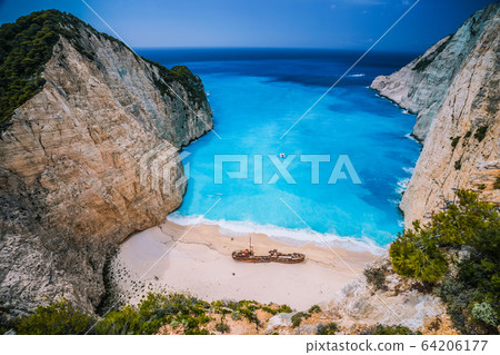 Shipwreck in Navagio beach. Azure turquoise sea water and sandy beach. Famous tourist visiting landmark on Zakynthos island, Greece Shipwreck in Navagio beach. Azure turquoise sea water and sandy beach. Famous tourist visiting landmark on Zakynthos island, Greece 64206177